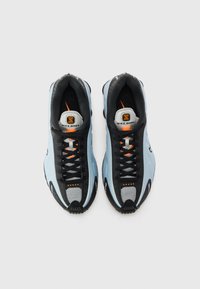 Sininen ja musta Nike Shox -kengät oransseilla yksityiskohdilla, katsottuna ylhäältä päin, yksinkertaisella valkoisella taustalla.