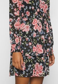 Blommig klänning i svart genomskinligt tyg med rosa och blå blommor, långa ärmar med smockade manschetter och en flerdelad kjoldesign.