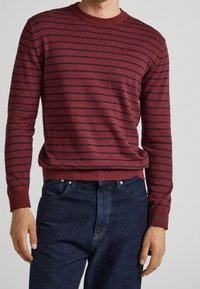 Röd och marinblå randig tröja med rund halsringning och ribbad mudd och nederkant, kombinerad med mörkblå jeans.