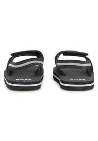 Μαύρα σαγιονάρες με δύο επάνω λουράκια σε γκρι και άσπρες ρίγες. Υφή στη σόλα και το λογότυπο της μάρκας ορατό στο πέλμα.