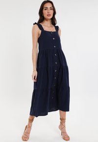 Abito midi blu navy con bottoni, design a strati e spalline a volant. Realizzato in tessuto morbido, presenta un corpino aderente e una gonna fluida.