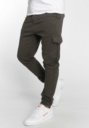 Ciemnoszare spodnie dresowe z miękkiego materiału, z bocznymi kieszeniami, slim fit i elastycznymi mankietami, w połączeniu z białymi sneakersami.