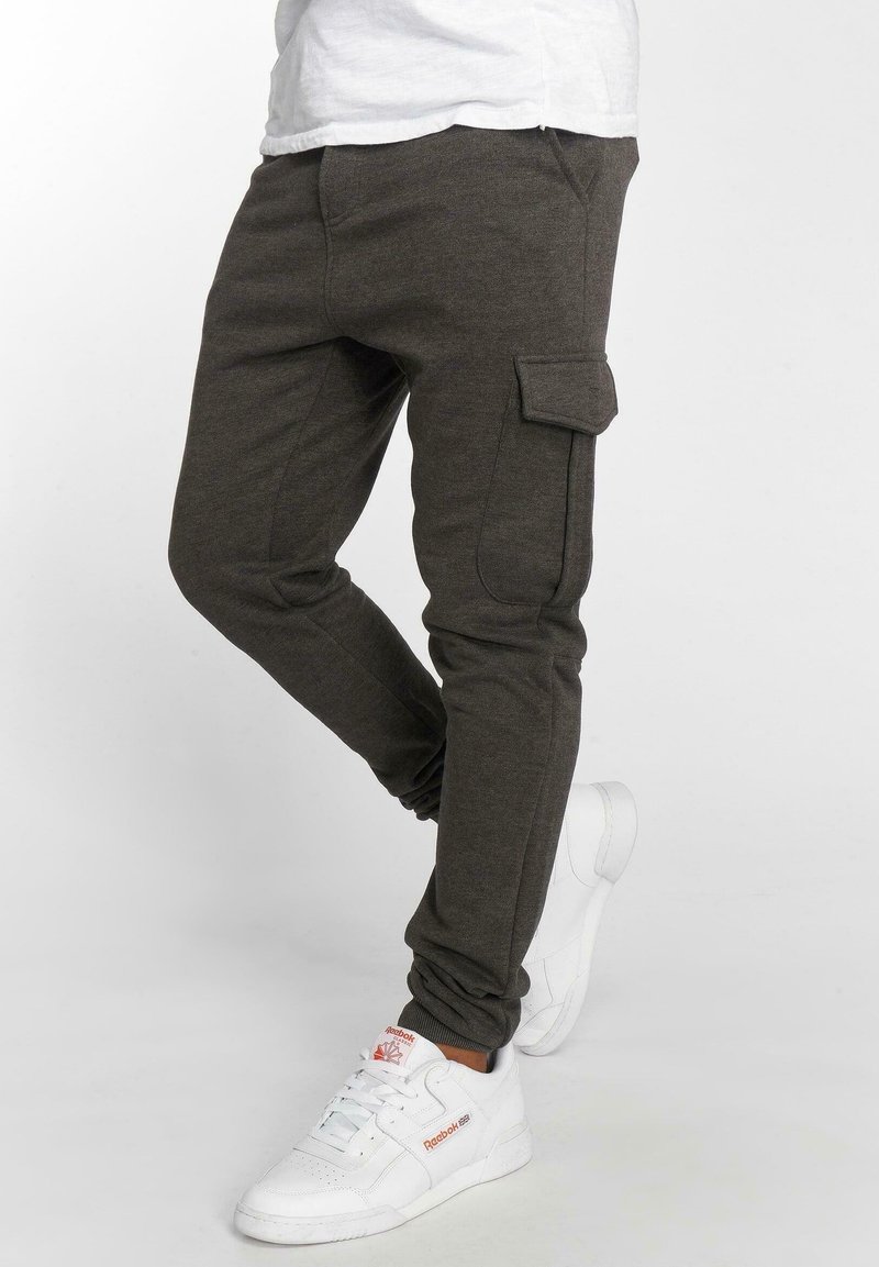 Ciemnoszare spodnie dresowe z miękkiego materiału, z bocznymi kieszeniami, slim fit i elastycznymi mankietami, w połączeniu z białymi sneakersami.