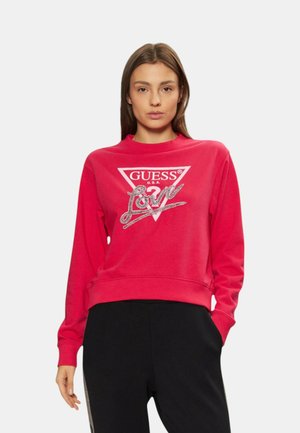 Sudadera roja con un logo triangular blanco que dice "GUESS U.S.A." y un diseño de "Love" en glitter plateado. Puños y dobladillo acanalados.
