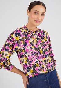 Blusa multicolore con motivo floreale, caratterizzata da un collo arricciato e chiusura a bottoni, realizzata in tessuto leggero. Maniche lunghe con polsini.