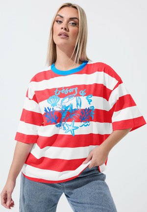 Lyshåret kvinde iført en oversized rød- og hvidstribet T-shirt med blåt havtema print og fransk tekst, kombineret med lyseblå jeans.