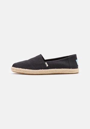 Chaussure espadrille en toile noire à enfiler avec semelle tressée beige et petite étiquette de marque en tissu sur le côté et le talon.