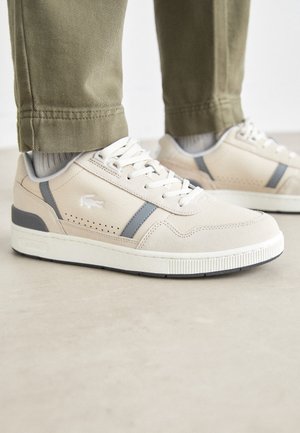 Beige Sneakers mit grauen Akzenten, Obermaterial aus strukturiertem Leder, runde Zehen und weiße Gummisohle. Mit Logo an der Seite und durchbrochenen Details.