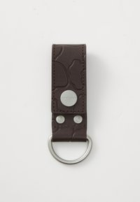 Porte-clés en cuir brun texturé avec un design embossé, boutons en métal argenté et attache en forme d'anneau métallique circulaire.