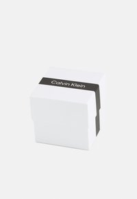 Hvit firkantet boks med en svart stripe med "Calvin Klein" tekst. Glatt overflate og skarpe kanter, designet for emballasje.