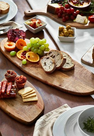 Taglieri assortiti di salumi con pane a fette, uva, agrumi, olive, formaggi, cracker e carni stagionate su un tavolo di legno.