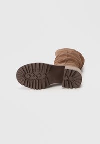 Brown suede ankle boot with a gathered design, featuring a textured rubber sole and prominent tread pattern for traction.