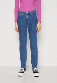 Blå denimjeans med slim fit, med femficksdesign och knäppning, kombinerat med svartvita sneakers.