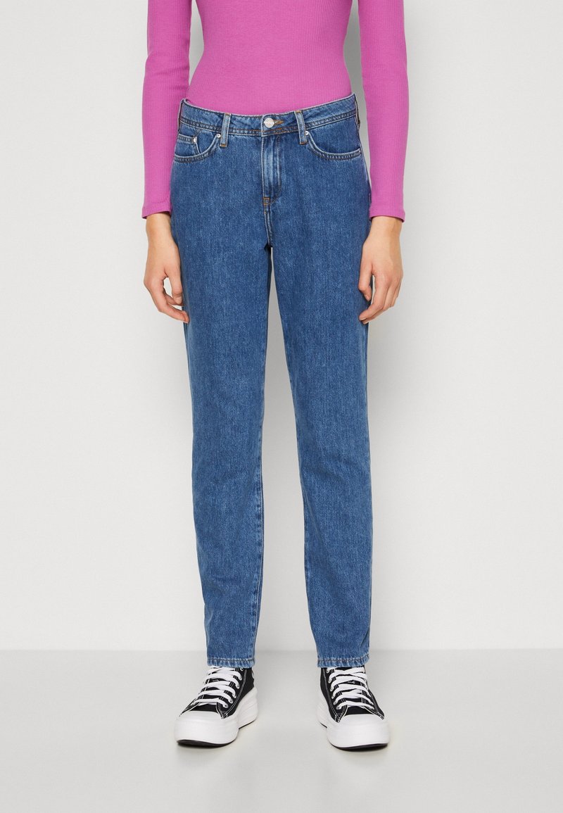 Blå denimjeans med slim fit, med femficksdesign och knäppning, kombinerat med svartvita sneakers.