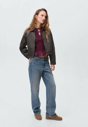 Chaqueta negra corta sobre una blusa de punto burdeos con dobladillo con volantes, combinada con jeans holgados azul claro y zapatos marrones sin cordones.
