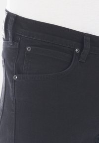 Jeans de denim negro con una textura suave, diseño estándar de cinco bolsillos y remaches de metal. Incluye una etiqueta de la marca en la cintura.