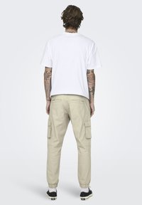 Witte katoenen t-shirt met korte mouwen, gecombineerd met beige cargobroek met zijzakken en elastische cuffs, gedragen met zwarte sneakers.