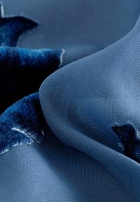 Tissu texturé bleu présentant une finition lisse avec un accent en velours, mettant en valeur des nuances de bleu dans un motif ondulé.