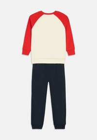 To-delt tøj sæt bestående af en cremefarvet sweatshirt med røde raglanærmer og marineblå joggerbukser. Lavet af blød bomuldsblanding.
