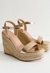 Sandali wedge metallici dorati con design aperto, piattaforma in juta intrecciata e due cinturini regolabili alla caviglia. Soletta di un rosa chiaro visibile.