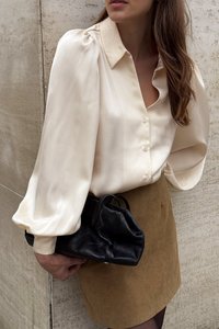 Cream satin blouse with puff sleeves, button-placket, paired with a brown suede skirt and a small black leather handbag.