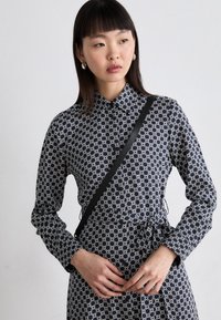 Vestito camicia a maniche lunghe con un motivo geometrico blu navy e bianco, colletto, vita con cordino e spallaccio nero. Tessuto di consistenza liscia.