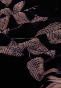 Tessuto nero con una texture morbida e vellutata che presenta un motivo floreale di foglie beige chiaro con dettagli fini.