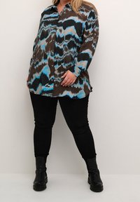 Skjorte med knapper og bølgemønster i blå, sort og brun, med lange ærmer og en afslappet pasform. Matchet med sorte skinny bukser og støvler.