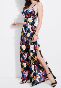 Blommig jumpsuit med spaghettiaxlar, svart bas och livfulla blommor i rosa, gult och blått. Har sidslitsar och knytbar midja.