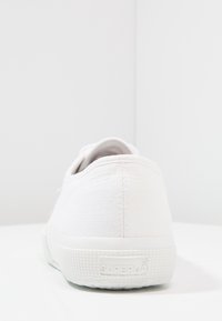 Vit canvas sneakers med texturerad ovandel, gummisula och präglad logotyp. Rund häl och enkelt design, lämplig för avslappnad användning.