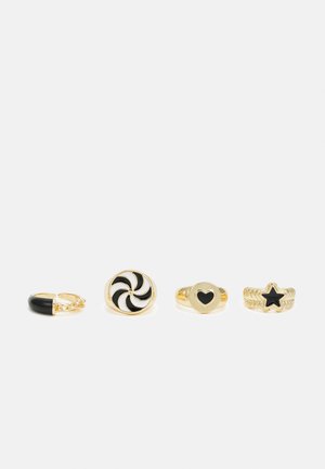 Quatro anéis: um anel de corrente de elos em ouro com um destaque preto, um anel de design espiral em ouro, um anel em forma de coração e um anel texturizado em forma de estrela.