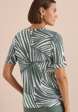 Woman with short brown hair wearing short-sleeve knit top with abstract black, white, and light green leaf pattern, shown from the back.