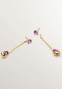 Pendientes de oro con una forma larga de gota de agua que tienen una gema de color púrpura profundo en la parte inferior, y pendientes de stareta con piedras púrpuras más pequeñas en la parte superior.
