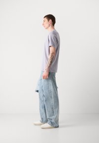 Light purple short-sleeve t-shirt paired with light blue wide-leg denim jeans and white sneakers; features a subtle logo on the chest.