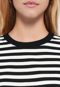 Μπλούζα με ασπρόμαυρες ρίγες και ριμπ ύφασμα στο λαιμό σε μαύρο χρώμα. Το υλικό φαίνεται απαλό και ελαστικό, με ομοιόμορφες οριζόντιες ρίγες.