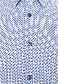 Koszula z krótkim rękawem z geometrycznym wzorem w kolorze niebieskim i białym, wykonana z gładkiej tkaniny, z czarnym guzikiem z przodu.