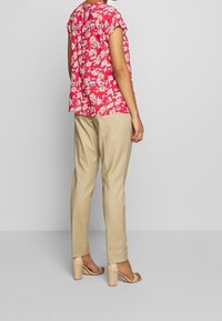 Rode bloempatron blouse met korte mouwen, gecombineerd met beige, tapered broek en huidskleurige hakken. Zachte stoftextuur, relaxte pasvorm.