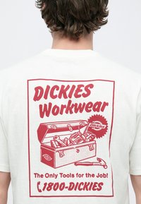 Λευκό T-shirt με μεγάλο κόκκινο γραφικό που απεικονίζει το κείμενο «DICKIES Workwear», εικονογράφηση εργαλείων και σχέδιο εργαλείου.