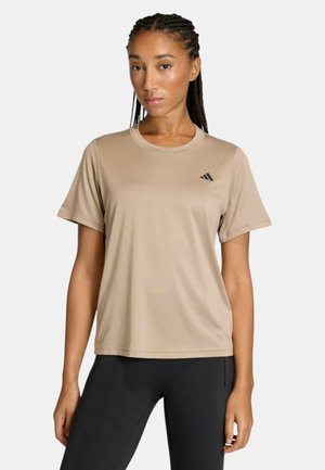 Giovane donna con capelli intrecciati, indossa una maglietta sportiva beige a maniche corte e leggings neri, su uno sfondo semplice.