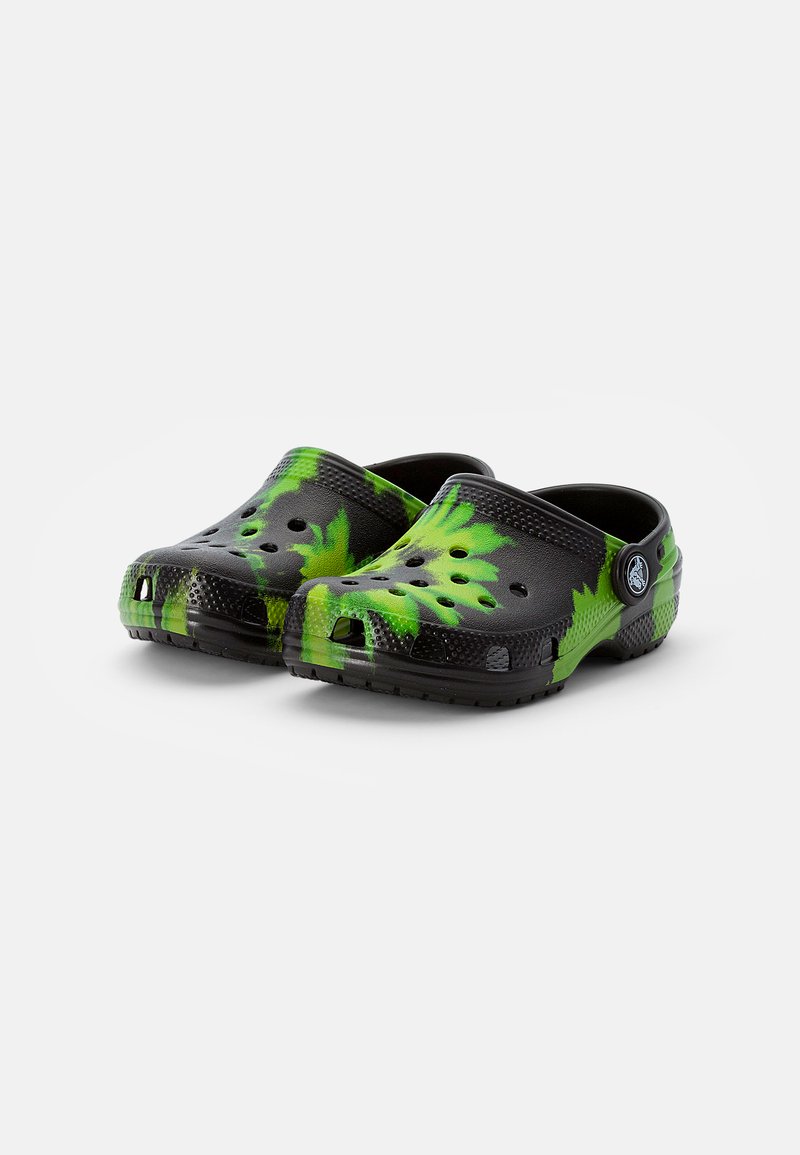 Zuecos negros y verdes con un patrón de hojas, hechos de material flexible, con orificios de ventilación y una correa trasera para un ajuste seguro.