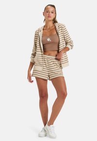 Conjunto de loungewear a rayas en beige y marrón que incluye una sudadera con cremallera, una camiseta de tirantes corta y pantalones cortos a juego. Mezcla de algodón, ajuste relajado.