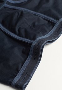 Tmavě modré látkové kraťasy s hladkým povrchem, zdobené kontrastním tmavě modrým prošíváním a elastickým pasem s vyraženým logem.