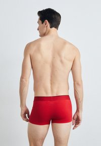 Piros boxer alsónadrág fekete derékszíjjal, testhez álló fazonú, sima tapintású és közepes hosszúságú, hátulról nézve.