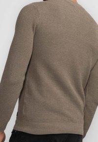Hellbraunes Strickpullover mit strukturiertem Muster, geripptem Halsausschnitt und Bündchen sowie geradem Saum. Der Stoff wirkt weich und warm.
