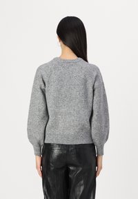 Grau gestrickter Pullover mit strukturierter Oberfläche, Raglanärmeln und geripptem Saum. Kombiniert mit schwarzen Lederhosen.