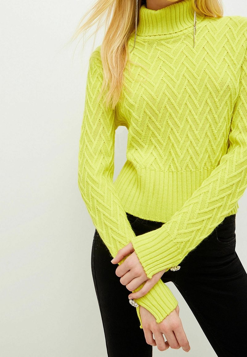 Yellow knitted sweater with a high collar, featuring a textured zigzag pattern and ribbed cuffs. Paired with black pants.