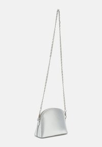 Sömlös handväska i silvermetall med en böjd form, strukturerad yta och en kedjestrap. Har en dragkedjestängning och diskret varumärkesdetalj.