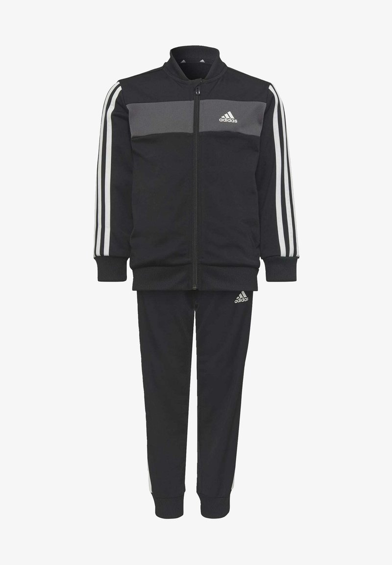 L'ensemble de survêtement noir comprend une veste zippée avec un panneau gris, des poignets côtelés et un pantalon assorti avec des rayures blanches sur les côtés et des accents de logo.