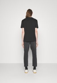 T-shirt noir à manches courtes avec une coupe droite, associé à un pantalon gris foncé et des baskets blanches, vu de dos.
