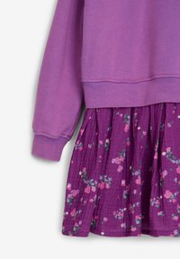 Lila Sweatshirt mit gerippten Bündchen, kombiniert mit einem gestuften Rock in lila mit floralem Druck, der kleine rosa und grüne Blumenmuster zeigt.